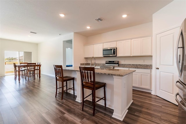 kitchen featuring dark wood finished floors, appliances with stainless steel finishes, light stone counters, and white cabinetry