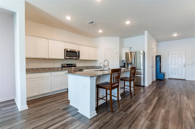 kitchen with white cabinets, dark wood-style floors, visible vents, appliances with stainless steel finishes, and a breakfast bar area