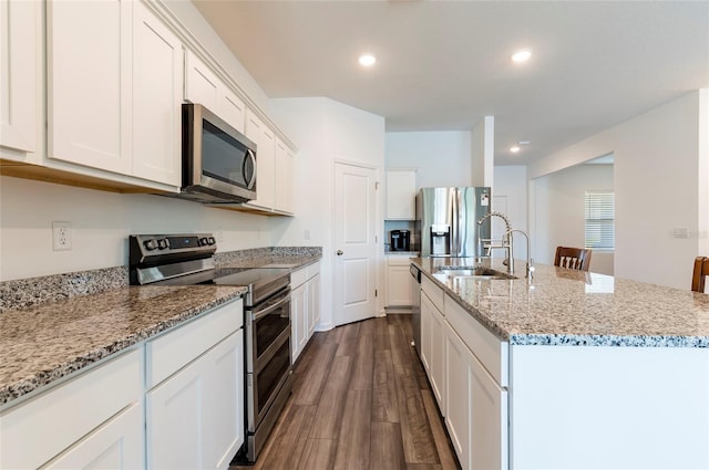 kitchen featuring a kitchen island with sink, stainless steel appliances, white cabinets, light stone countertops, and dark wood-style floors