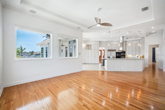 6202 Pasadena Point Blvd, Gulfport, FL 33707 - unfurnished living room featuring a raised ceiling, light wood-style flooring, ceiling fan, crown molding, and baseboards