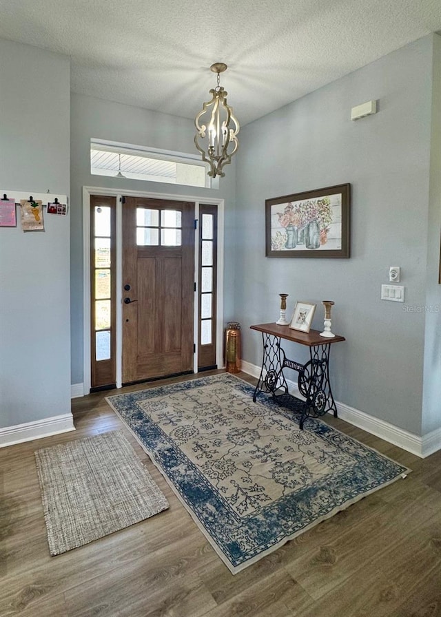foyer with a textured ceiling, baseboards, a chandelier, and wood finished floors
