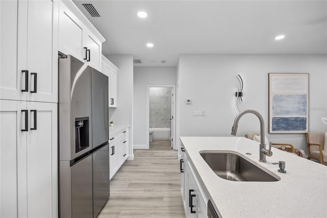 13117 4th St E, Madeira Beach, FL 33708 - kitchen featuring stainless steel refrigerator with ice dispenser, a sink, white cabinetry, light wood-type flooring, and light stone counters