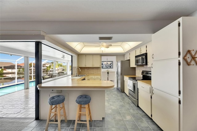 927 Golf Island Dr, Apollo Beach, FL 33572 - kitchen with appliances with stainless steel finishes, decorative backsplash, a peninsula, light countertops, and a tray ceiling