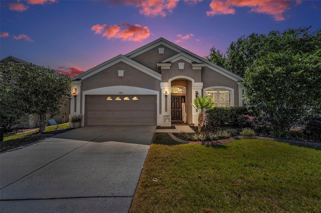 view of front of property with a yard, an attached garage, driveway, and stucco siding