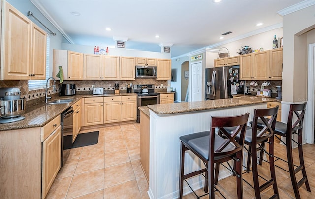 kitchen featuring light brown cabinets, a kitchen bar, tasteful backsplash, a sink, and appliances with stainless steel finishes