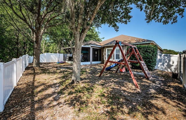 view of yard featuring a sunroom, a fenced backyard, and a playground