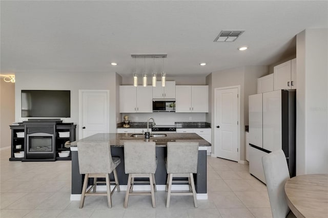 kitchen featuring a sink, a kitchen breakfast bar, freestanding refrigerator, white cabinetry, and visible vents