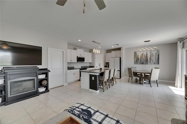 kitchen featuring freestanding refrigerator, a sink, dark countertops, a kitchen breakfast bar, and a ceiling fan