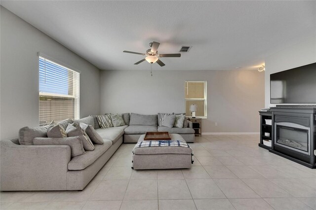 living room featuring light tile patterned flooring, ceiling fan, visible vents, and baseboards