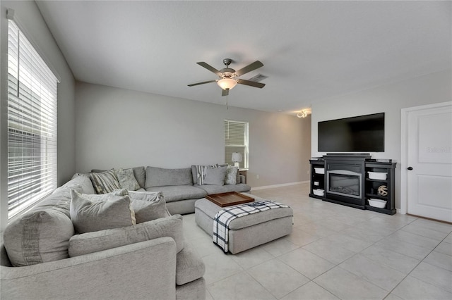 living room with a glass covered fireplace, a ceiling fan, baseboards, light tile patterned floors, and visible vents