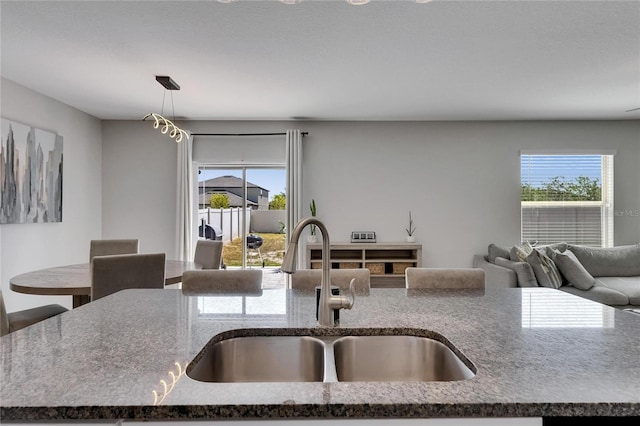 kitchen with hanging light fixtures, a sink, a kitchen island with sink, dark stone countertops, and open floor plan