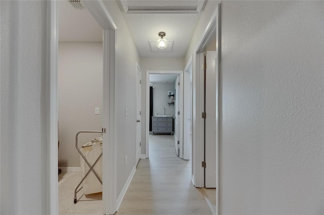 corridor with baseboards, attic access, light wood-style flooring, and visible vents