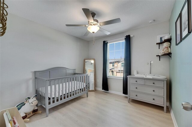 bedroom featuring baseboards, a crib, and light wood-style flooring