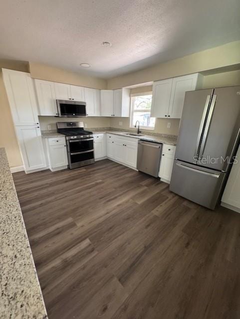 kitchen featuring stainless steel appliances, a sink, white cabinetry, light stone countertops, and dark wood-type flooring