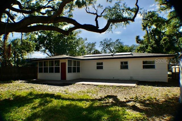 rear view of property with a yard, roof mounted solar panels, a patio, and fence