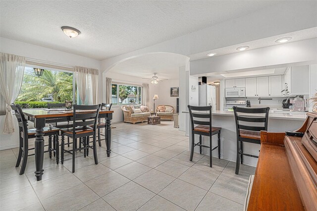 dining area featuring a ceiling fan, arched walkways, a textured ceiling, and light tile patterned flooring