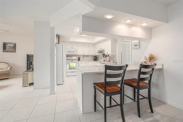 kitchen featuring light countertops, white appliances, a peninsula, a breakfast bar area, and white cabinetry