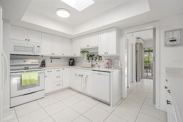 kitchen featuring a tray ceiling, light countertops, a sink, white appliances, and a skylight