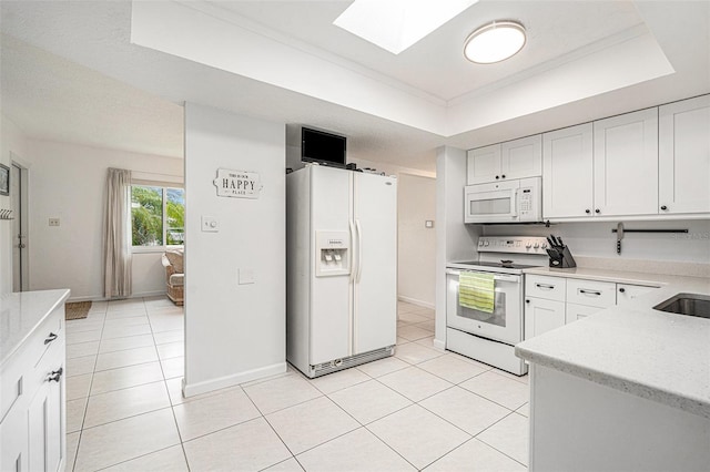 kitchen with a raised ceiling, a skylight, light tile patterned floors, and white appliances