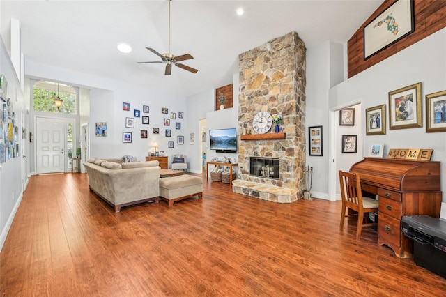 living room featuring high vaulted ceiling, a stone fireplace, a ceiling fan, baseboards, and wood finished floors