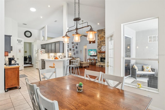 dining room with light tile patterned flooring, high vaulted ceiling, a stone fireplace, recessed lighting, and visible vents