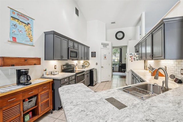 kitchen with decorative backsplash, a towering ceiling, a sink, appliances with stainless steel finishes, and light tile patterned floors