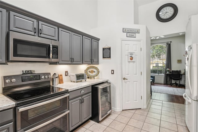kitchen featuring gray cabinets, appliances with stainless steel finishes, light tile patterned floors, baseboards, and wine cooler