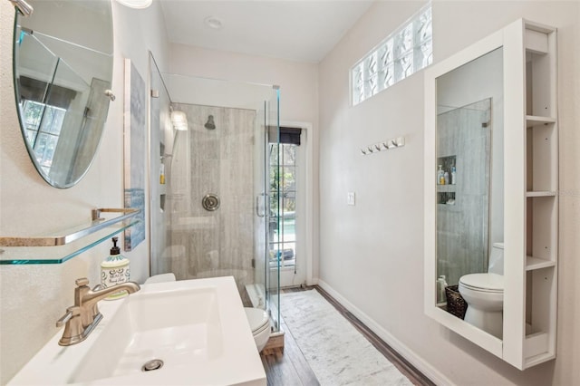 bathroom with wood finished floors, toilet, baseboards, a sink, and a stall shower