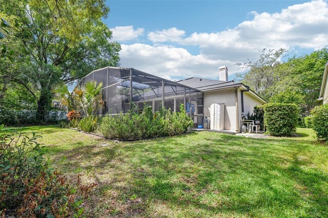 rear view of property featuring a yard, a chimney, a lanai, and stucco siding