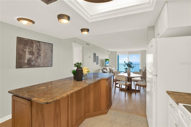 9 Haig Pl Unit 510, Dunedin, FL 34698 - kitchen featuring freestanding refrigerator, white cabinetry, dark stone counters, a kitchen island, and a tray ceiling