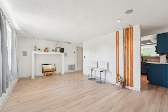 unfurnished living room with light wood finished floors, visible vents, a fireplace, and a sink
