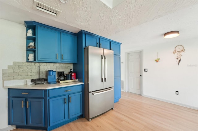 kitchen featuring blue cabinets, decorative backsplash, light wood-type flooring, visible vents, and freestanding refrigerator