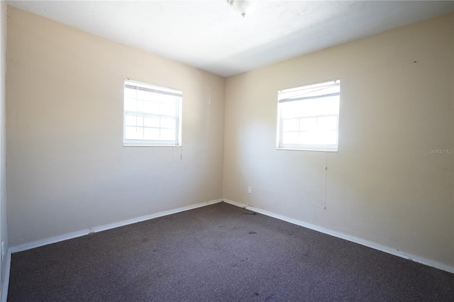 empty room featuring dark colored carpet, a wealth of natural light, and baseboards