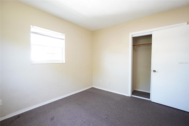 unfurnished bedroom featuring dark carpet, baseboards, and a closet