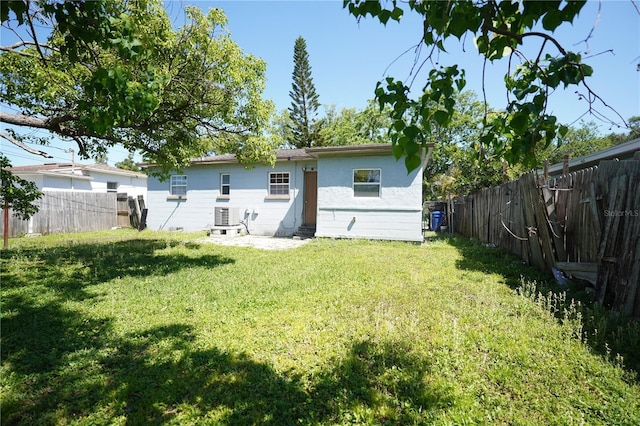 rear view of house featuring a fenced backyard, entry steps, central air condition unit, stucco siding, and a lawn