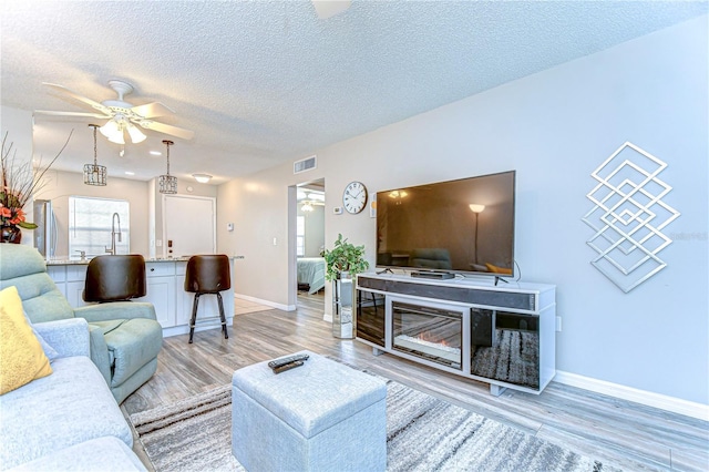 13870 Oakwood Ln Unit 13870, Seminole, FL 33776 - living room featuring a ceiling fan, a textured ceiling, light wood-type flooring, baseboards, and visible vents