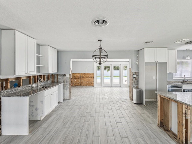 kitchen with white cabinets, light wood finished floors, open shelves, visible vents, and dark stone counters