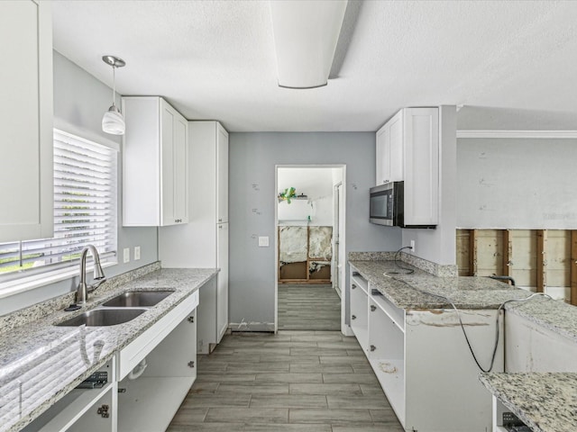 kitchen featuring stainless steel microwave, a textured ceiling, white cabinetry, and a sink