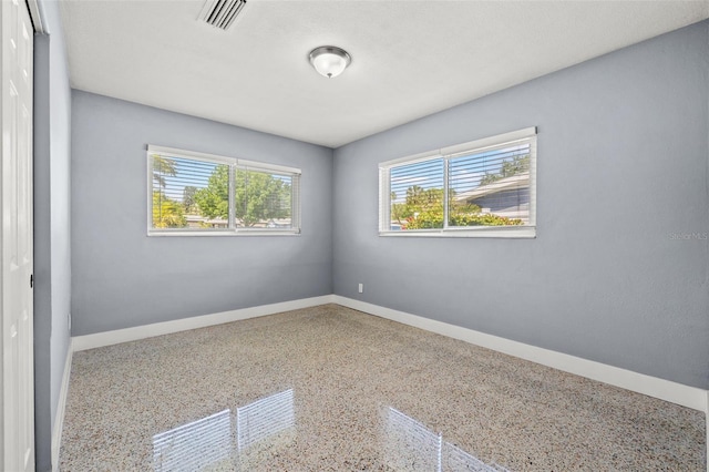 empty room featuring speckled floor, visible vents, and baseboards