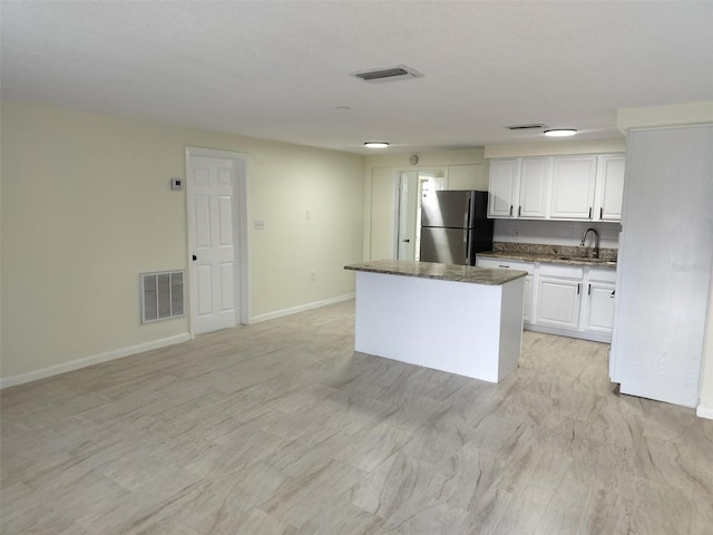 kitchen with a center island, a sink, visible vents, and freestanding refrigerator