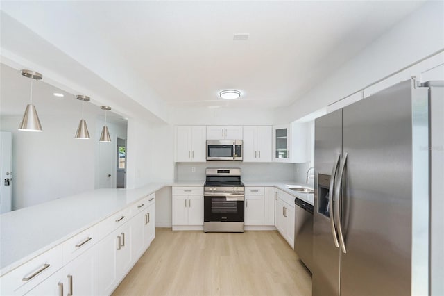 kitchen with appliances with stainless steel finishes, light wood-style floors, white cabinets, light countertops, and a sink