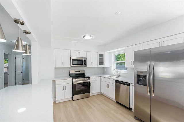 kitchen with appliances with stainless steel finishes, a sink, light wood-type flooring, light countertops, and white cabinetry
