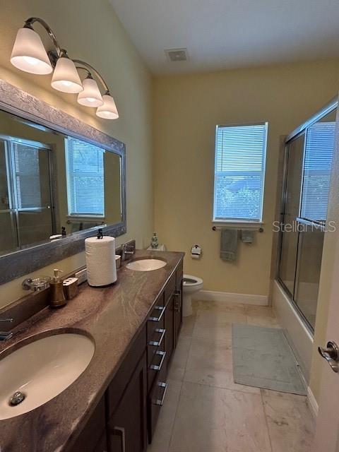 17127 Brown Rd, Odessa, FL 33556 - bathroom featuring toilet, double vanity, tile patterned flooring, bath / shower combo with glass door, and baseboards
