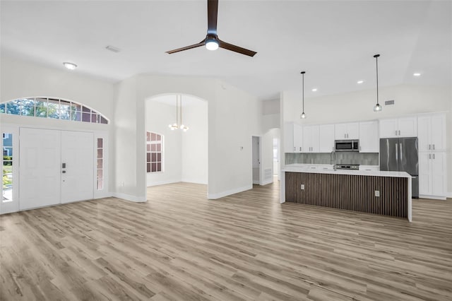 1135 Wyndham Lakes Dr, Odessa, FL 33556 - kitchen featuring open floor plan, light wood finished floors, arched walkways, appliances with stainless steel finishes, and high vaulted ceiling