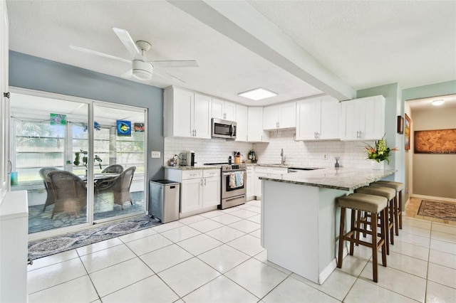 1751 Ashton Abbey Rd, Clearwater, FL 33755 - kitchen with stainless steel appliances, a peninsula, light stone counters, decorative backsplash, and white cabinets