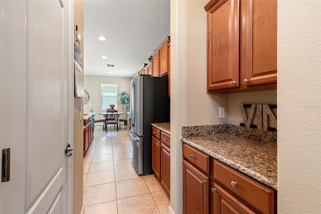 10617 Lucaya Dr, Tampa, FL 33647 - kitchen featuring freestanding refrigerator, brown cabinetry, light stone counters, and light tile patterned floors