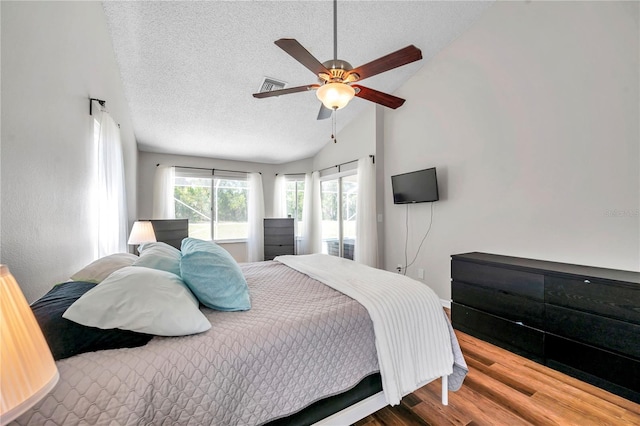 bedroom featuring wood finished floors, vaulted ceiling, visible vents, and a textured ceiling