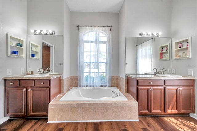 bathroom with two vanities, a garden tub, wood finished floors, and a sink
