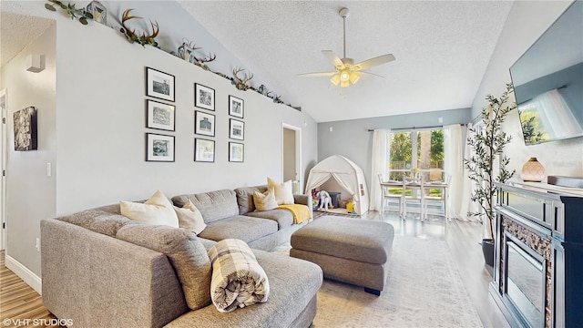 living room featuring vaulted ceiling, a textured ceiling, baseboards, ceiling fan, and wood finished floors