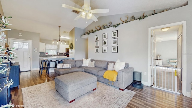 living room with baseboards, wood finished floors, ceiling fan with notable chandelier, and lofted ceiling